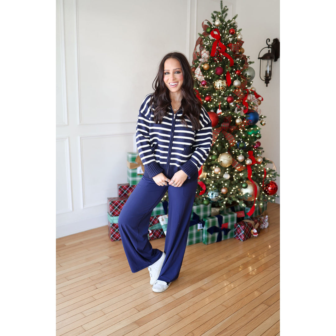 Woman in a striped sweater and blue pants standing in front of a decorated Christmas tree.