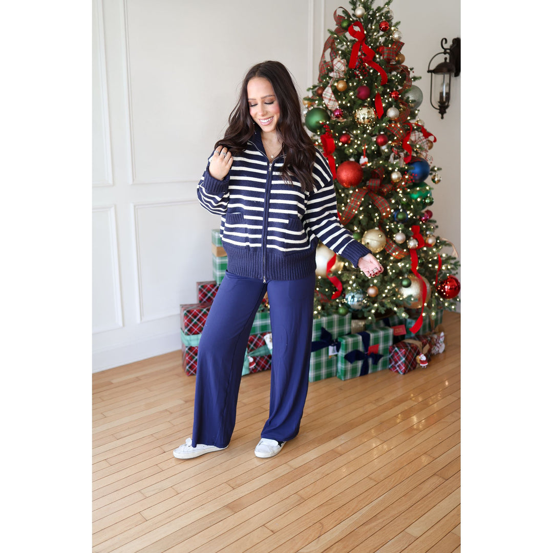 Woman in a striped sweater and blue pants standing in front of a decorated Christmas tree.