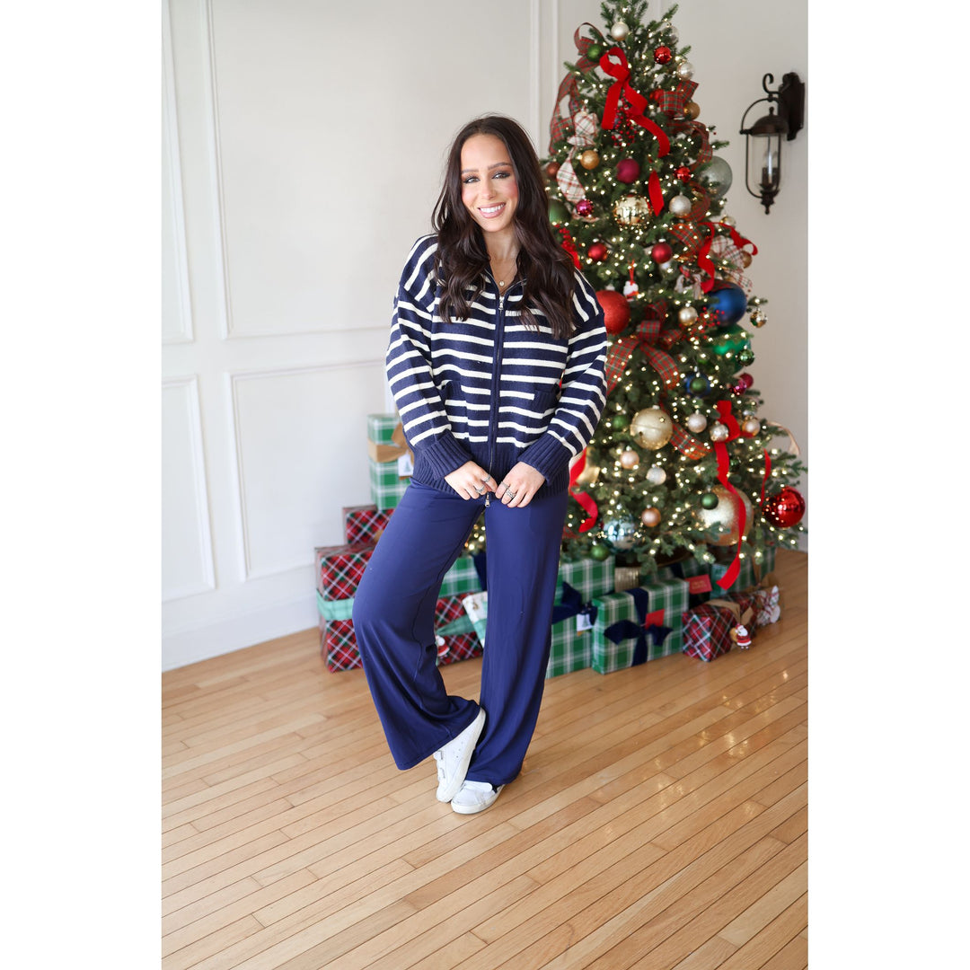 Woman in a striped sweater and blue pants standing in front of a decorated Christmas tree.