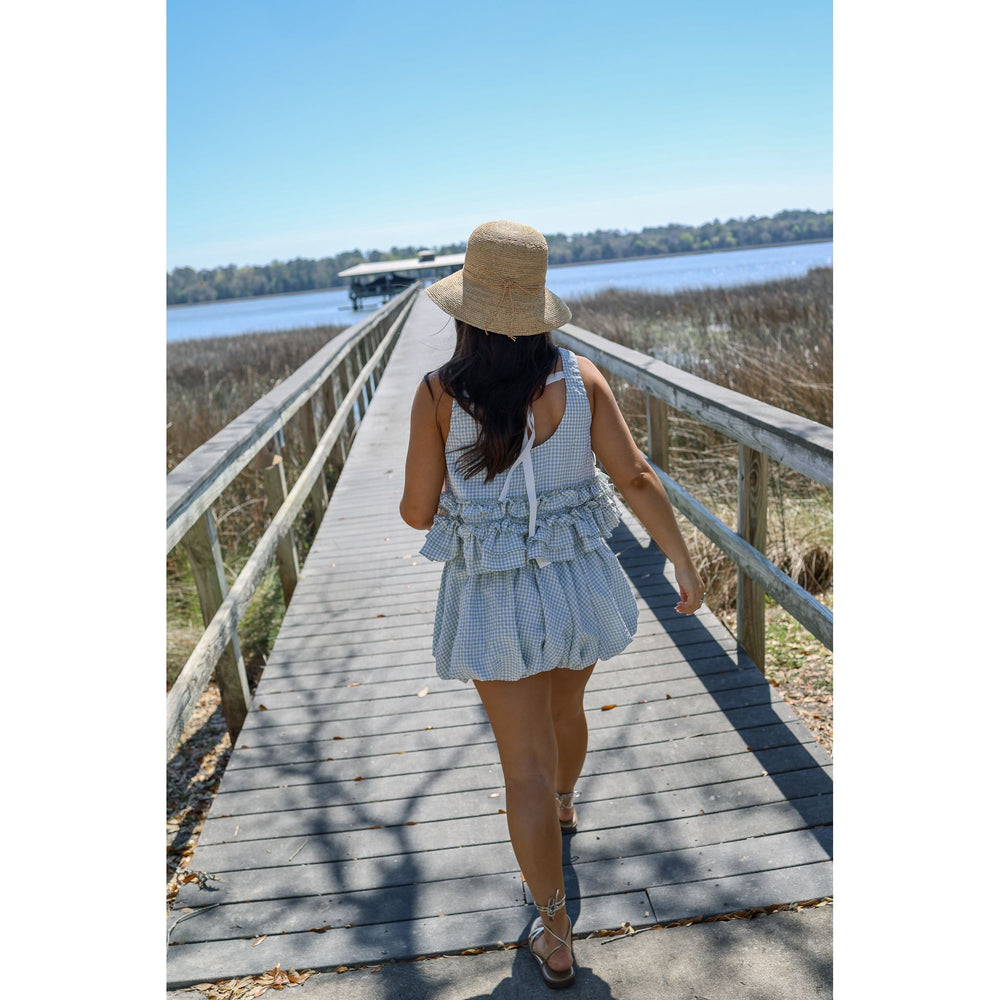 Woman walking on a wooden boardwalk by a lake, wearing a light blue set  and straw hat.