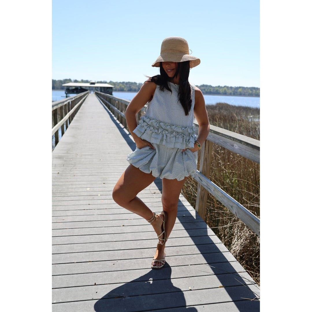 Woman in a light blue set and hat standing on a wooden dock by a body of water.