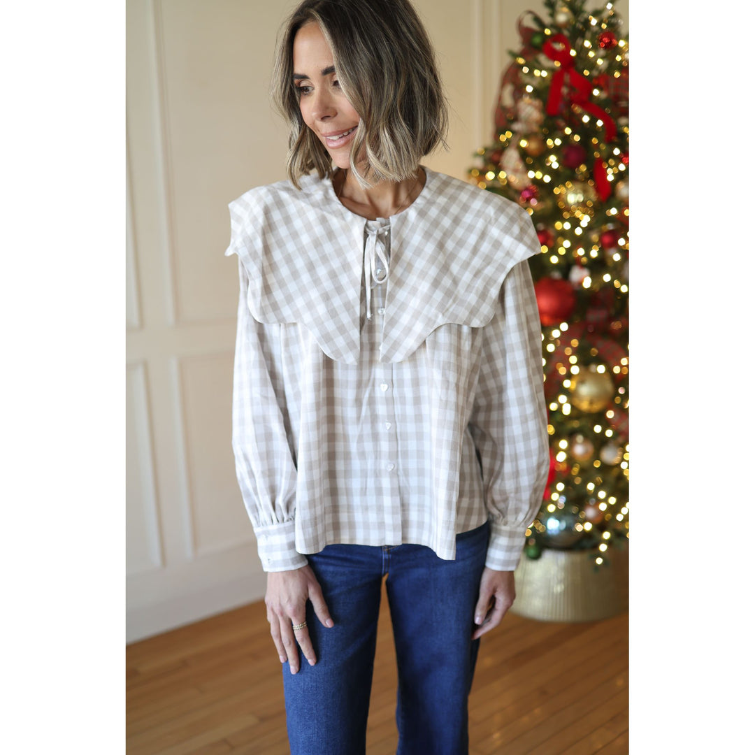Woman wearing a plaid blouse with ruffled shoulders in front of a decorated Christmas tree.