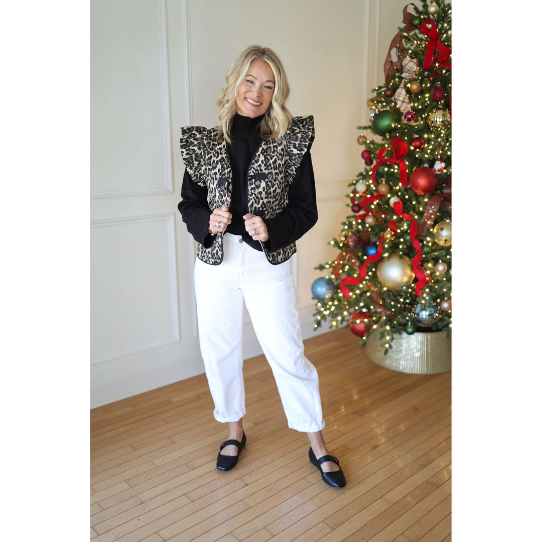 Woman wearing a leopard print vest and black top in front of a decorated Christmas tree.