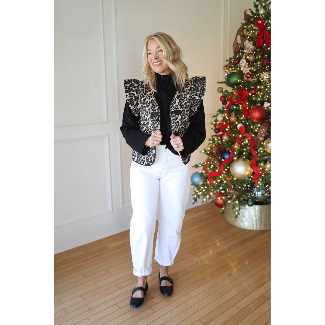 Woman in a stylish  leopard vest standing in front of a Christmas tree.