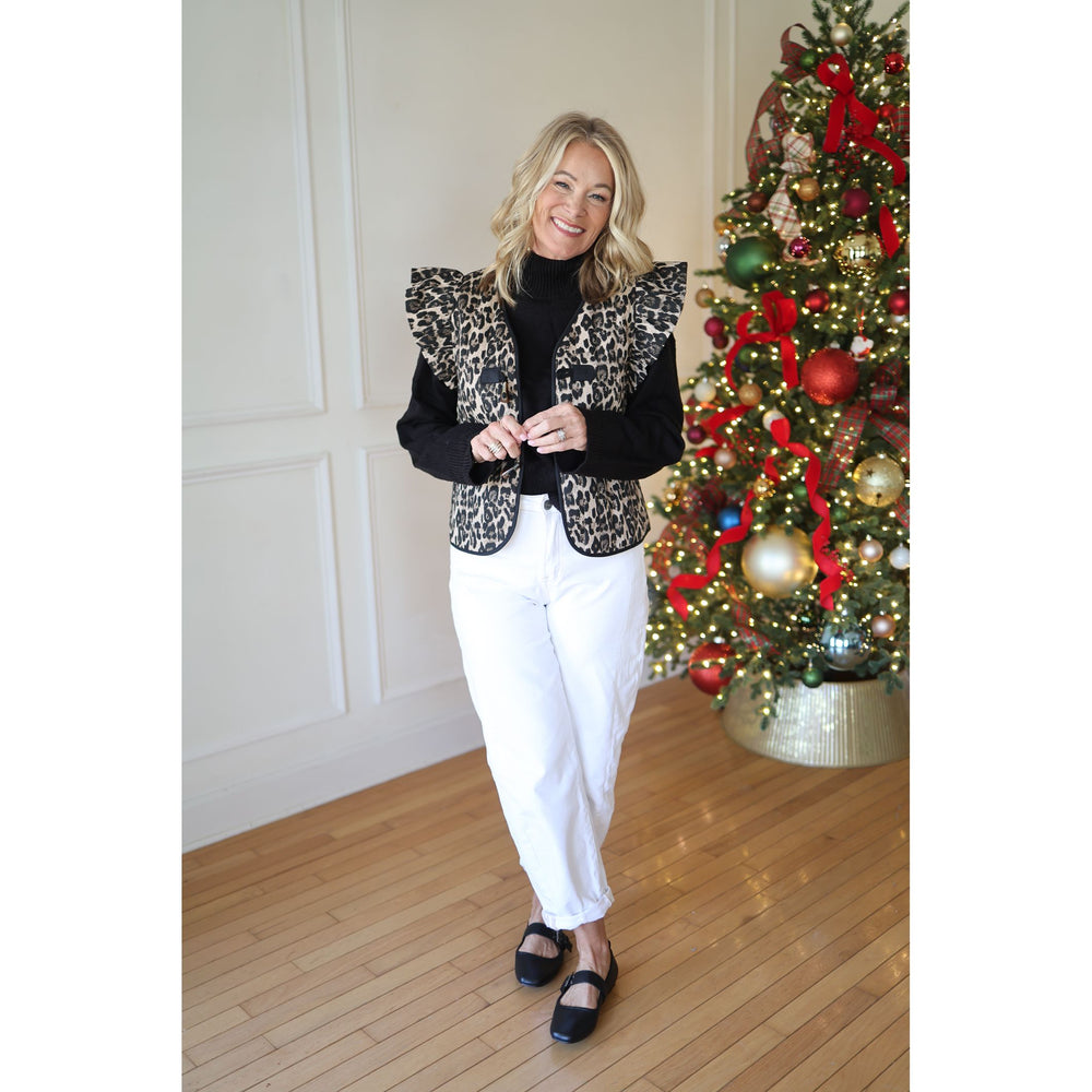 Woman in a leopard print vest standing in front of a decorated Christmas tree.