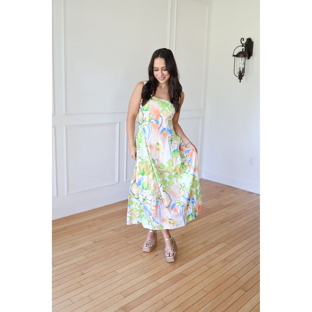 Woman wearing a floral dress standing in a room with wooden flooring and white walls.