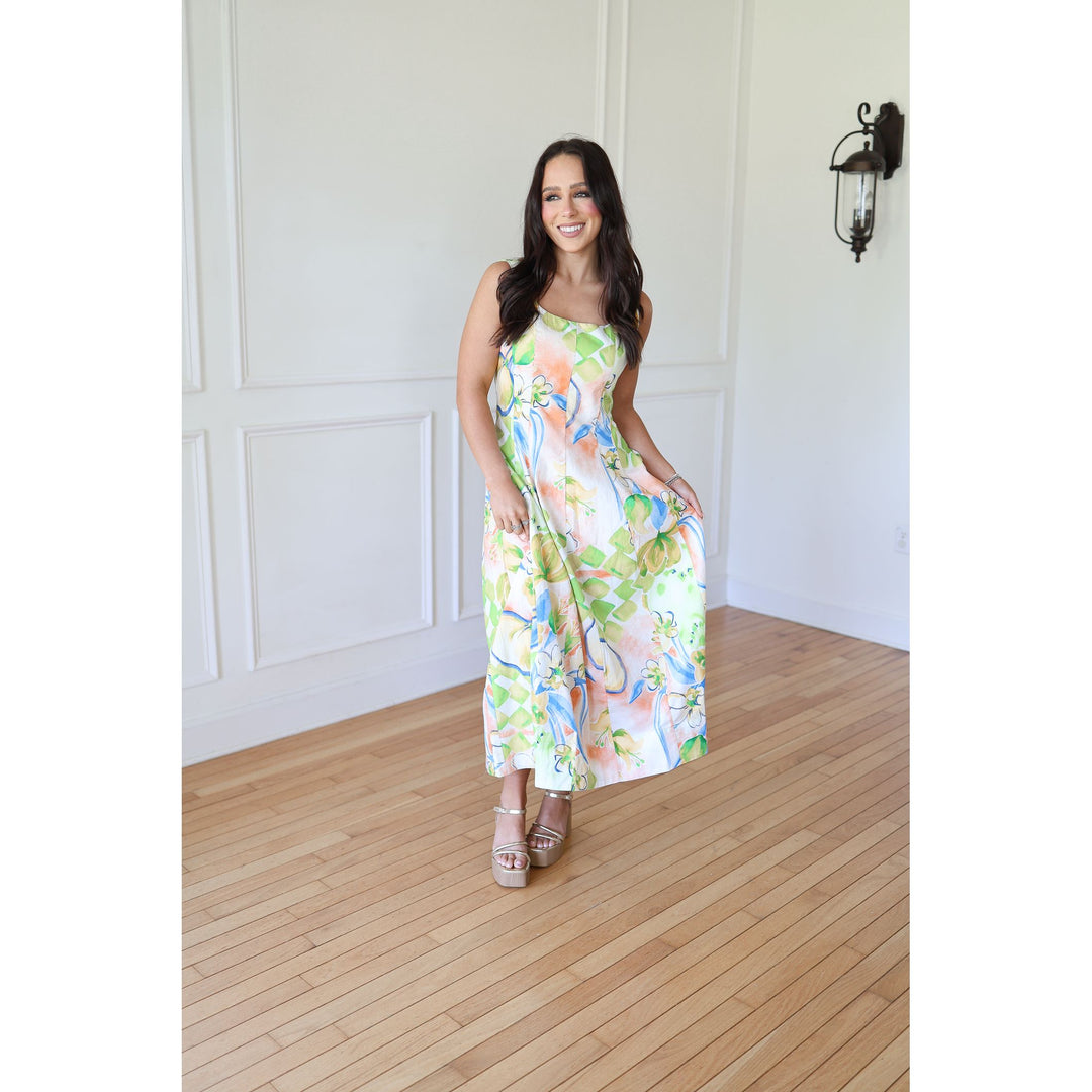 Woman in a floral dress standing in a room with wooden flooring and white walls.