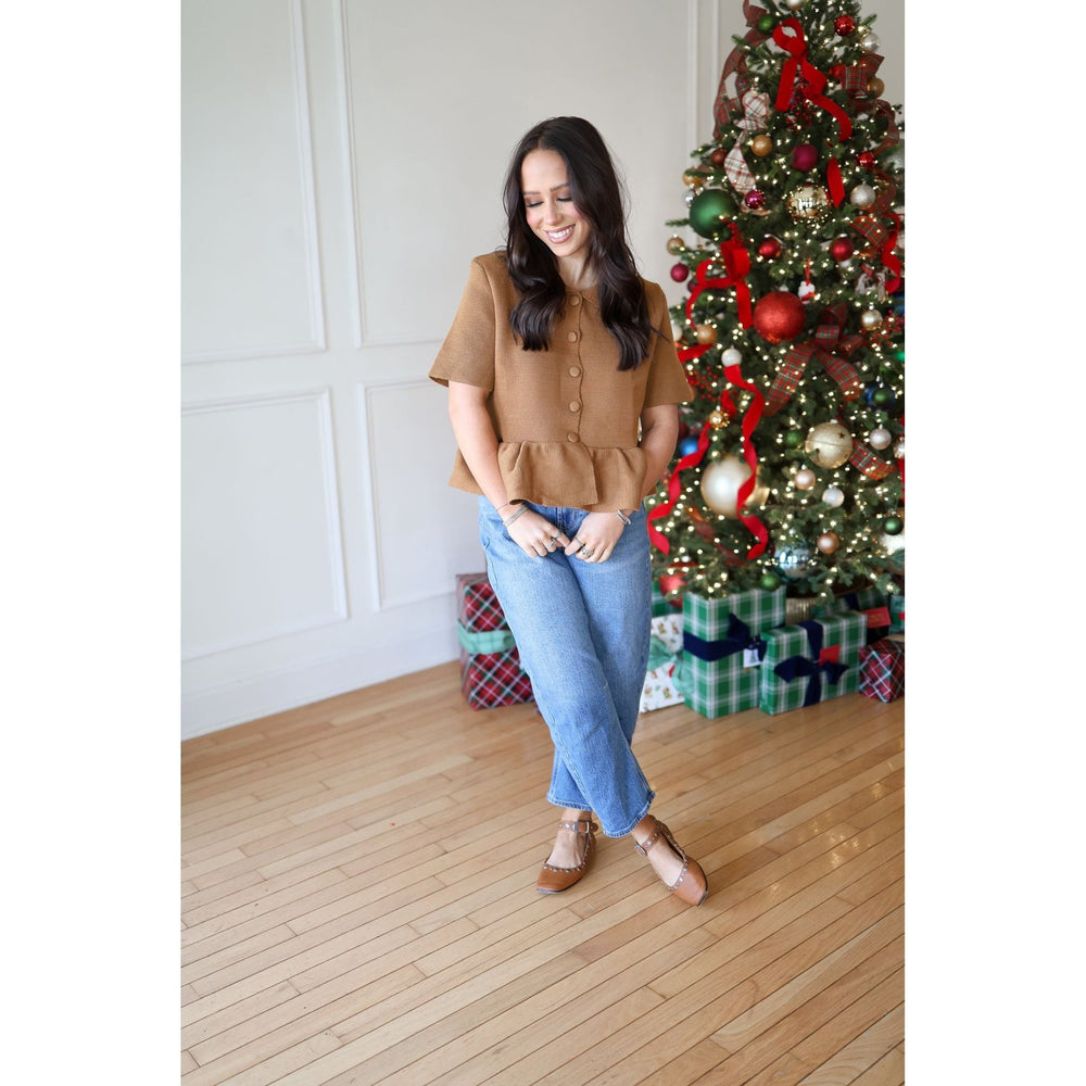 Woman standing in front of a decorated Christmas tree wearing a brown top and blue jeans.
