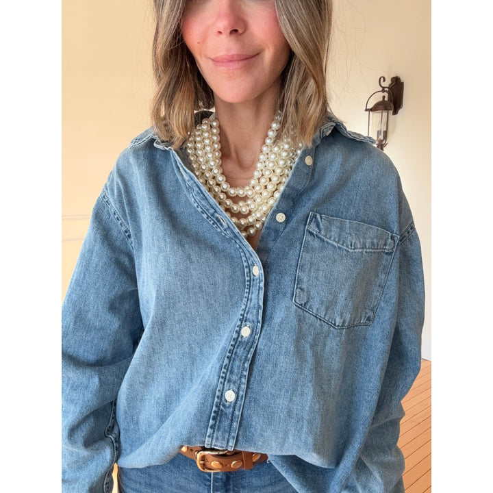 Person wearing a blue denim shirt with layered pearl necklace against a neutral background