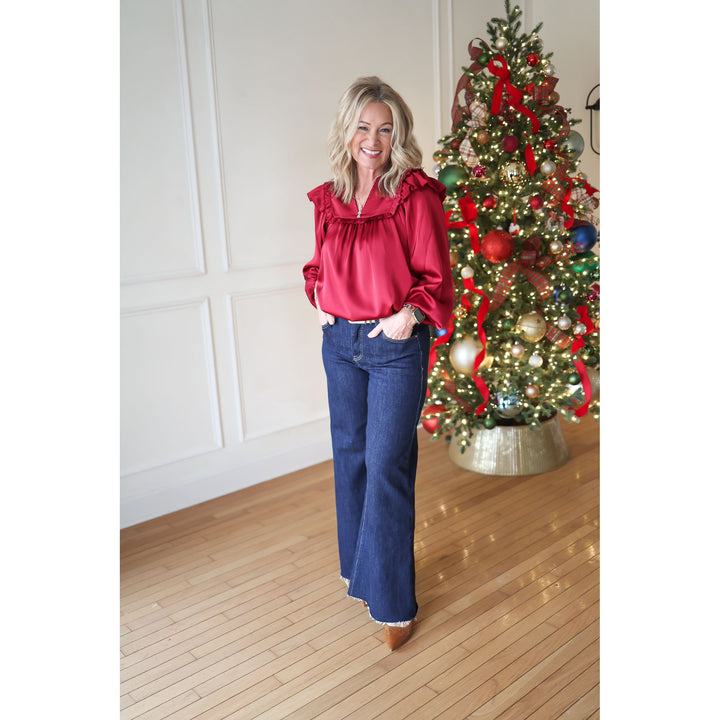 Woman in a red blouse and blue jeans standing in front of a decorated Christmas tree.