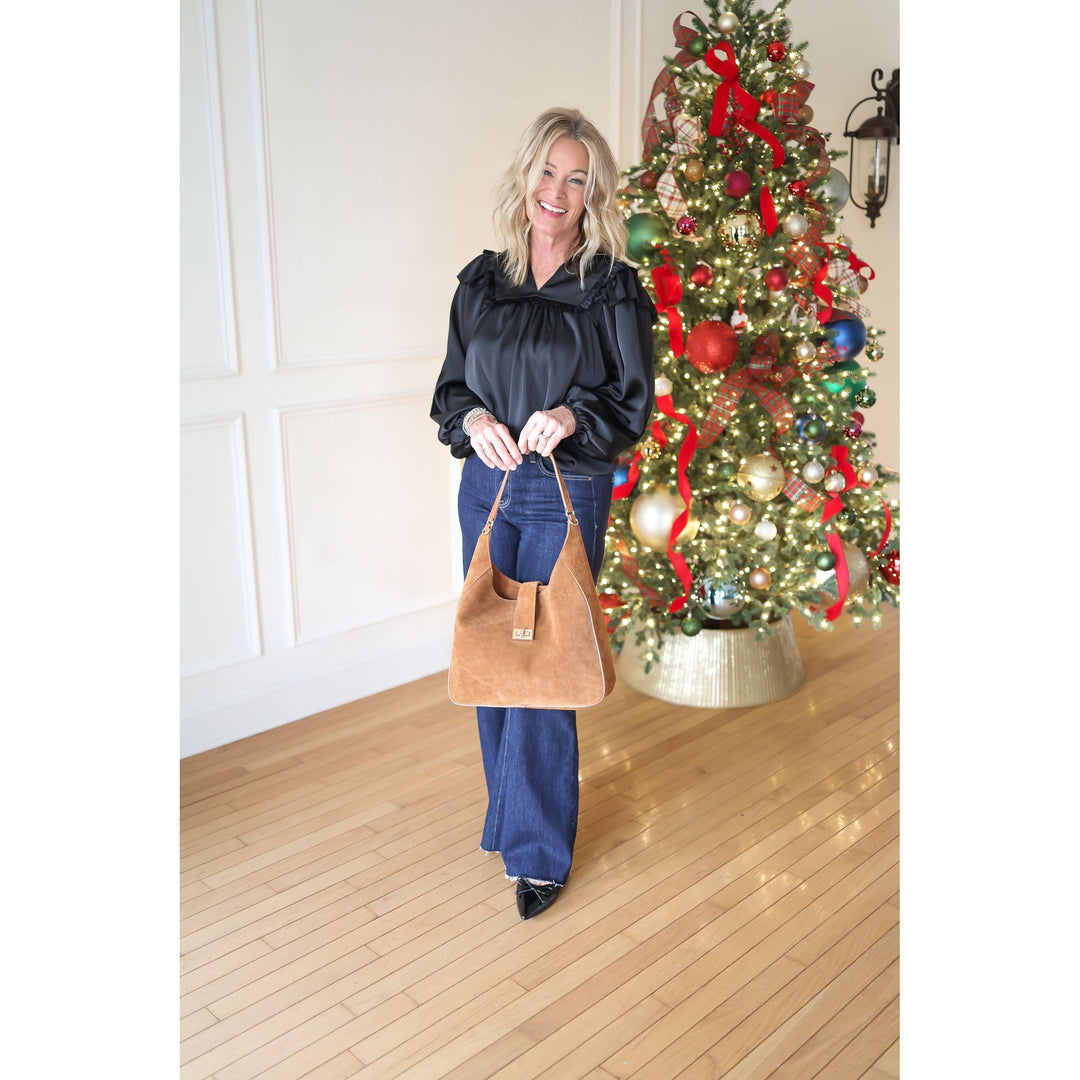 Woman holding a brown handbag in front of a decorated Christmas tree.