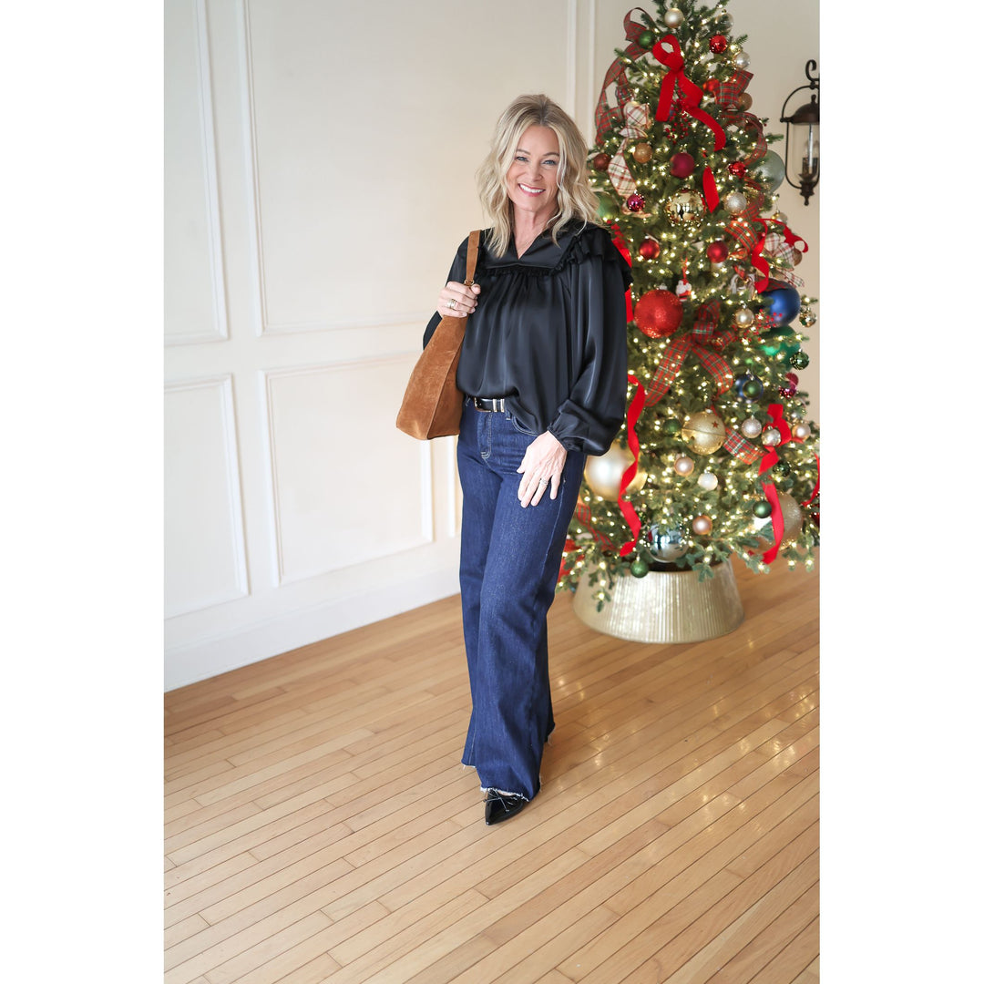 Woman in black top and blue jeans standing in front of a decorated Christmas tree.