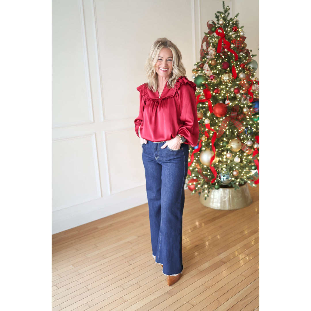 Woman in a red blouse and blue jeans standing in front of a decorated Christmas tree.