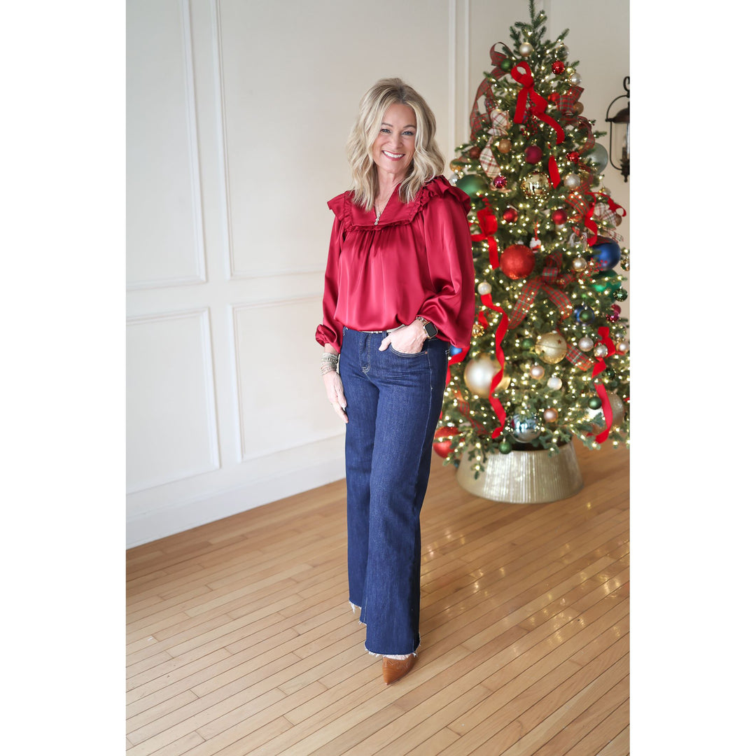 Woman in a red blouse and blue jeans standing in front of a decorated Christmas tree.
