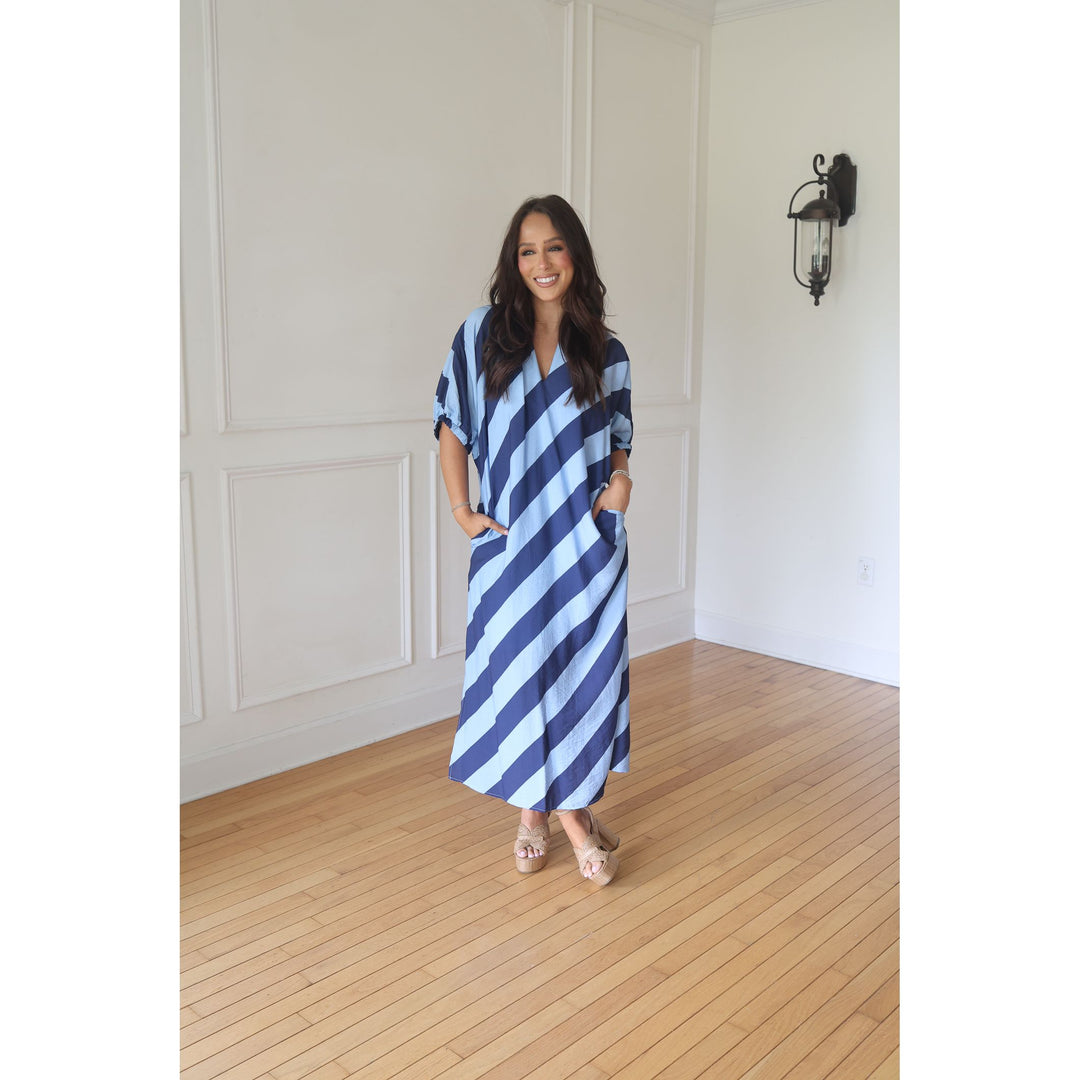 Woman wearing a blue and white striped dress standing in a room with wooden flooring and white walls.