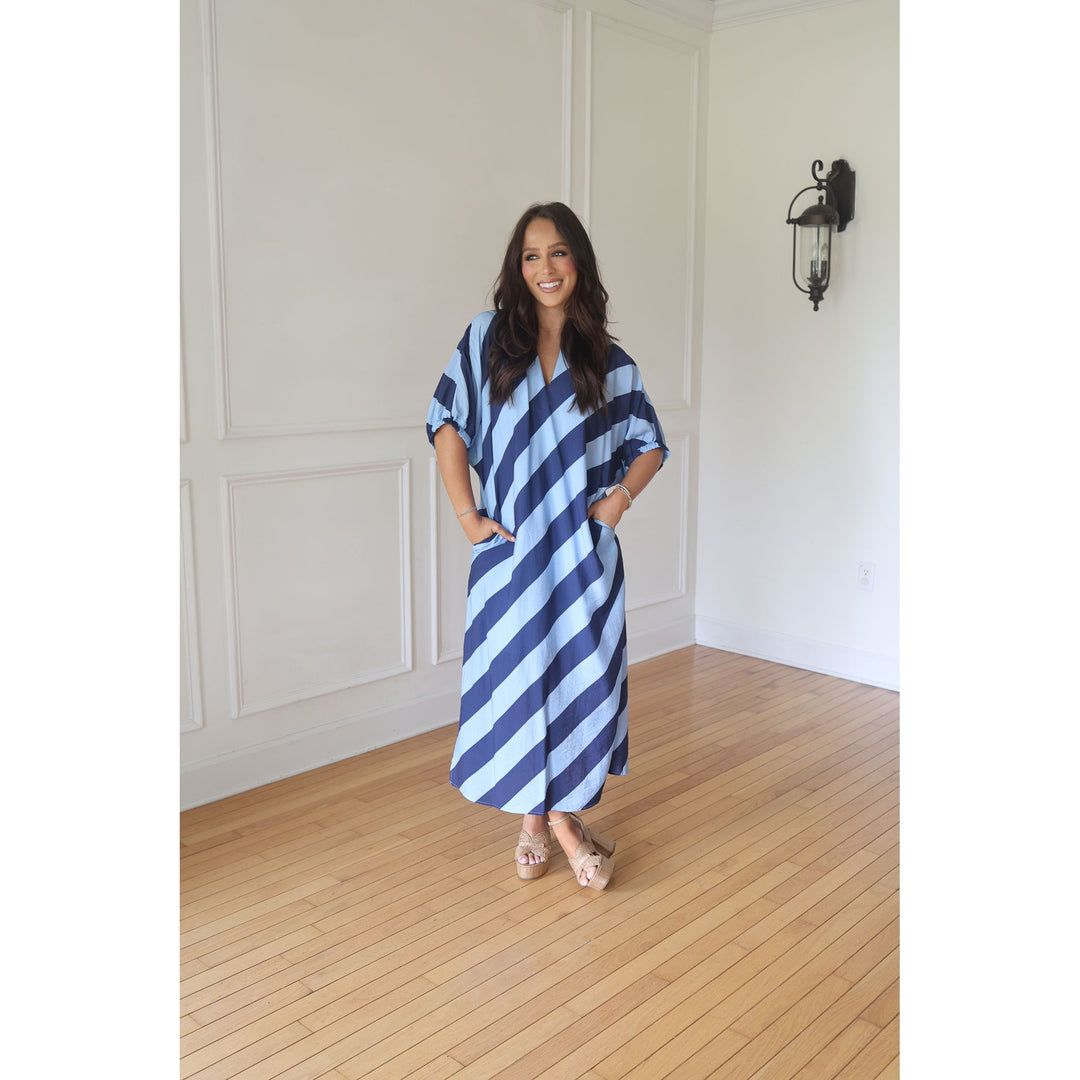 Woman wearing a blue and white striped dress standing in a room with wooden flooring and white walls.