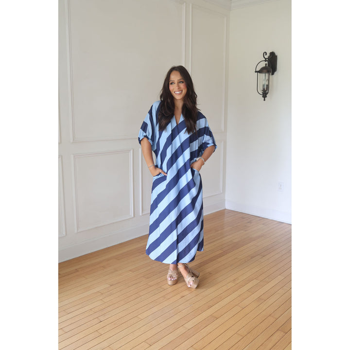 Woman wearing a blue and white striped dress standing in a room with wooden flooring and white walls.
