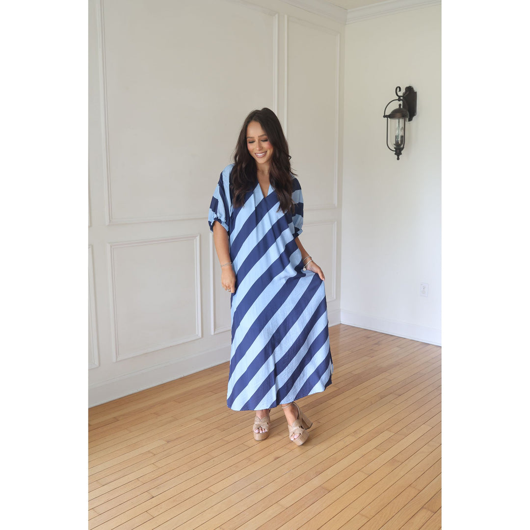 Woman wearing a blue and white striped dress in a room with wooden flooring and white walls.