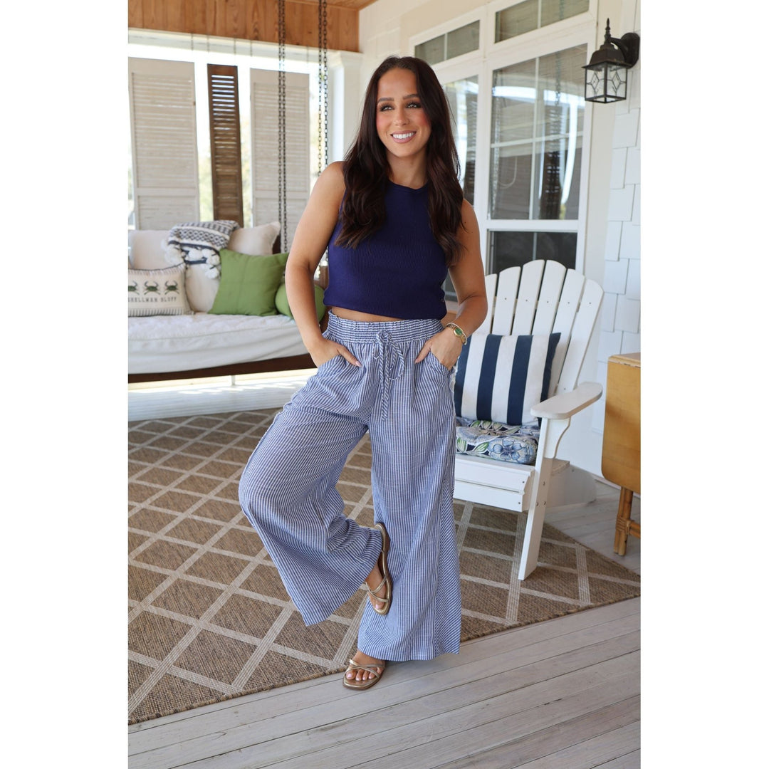 Woman in a blue top and striped pants standing on a porch.