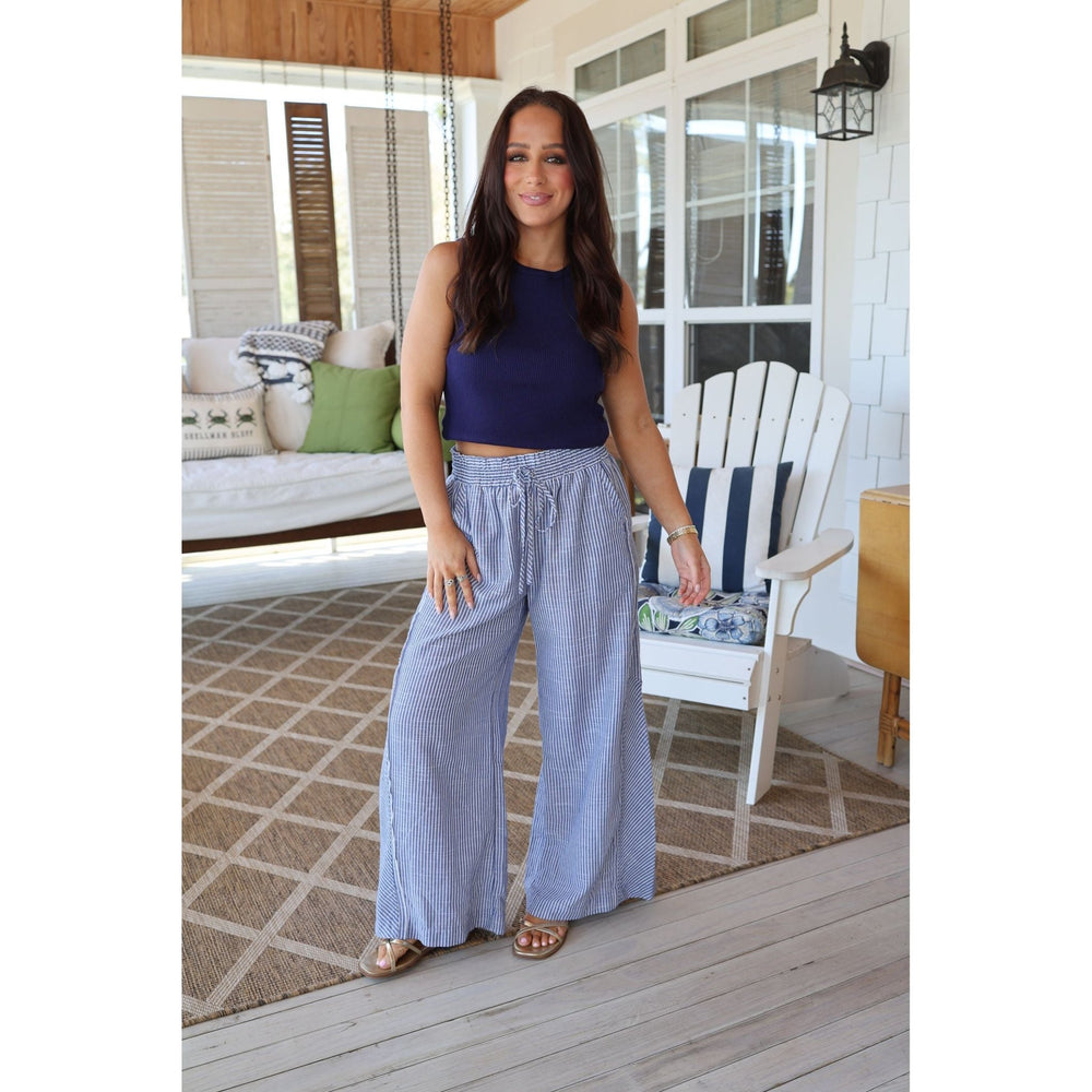 Woman standing on a porch wearing a blue top and light blue pants.