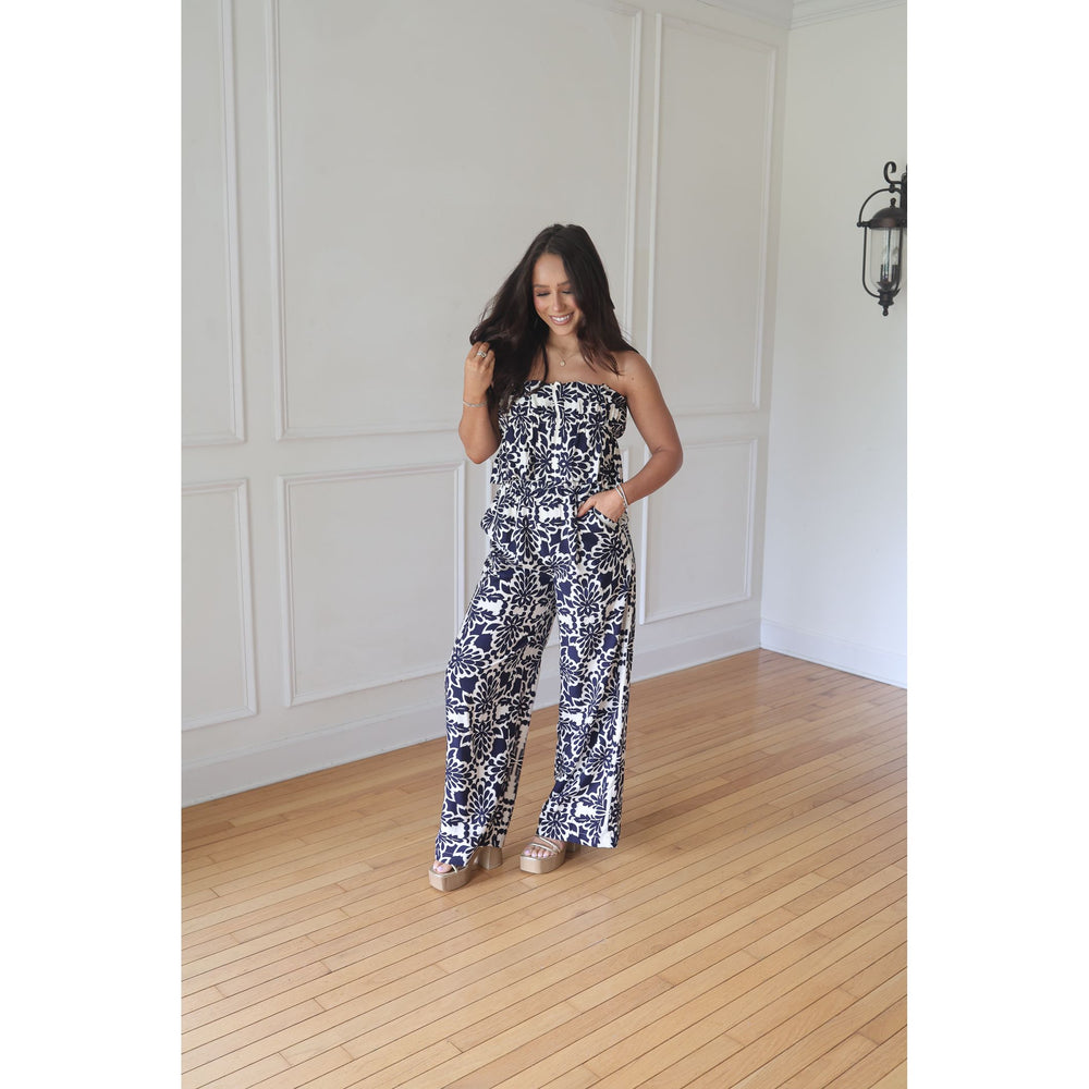 Woman wearing a black and white patterned strapless jumpsuit in a room with wooden flooring and white walls.