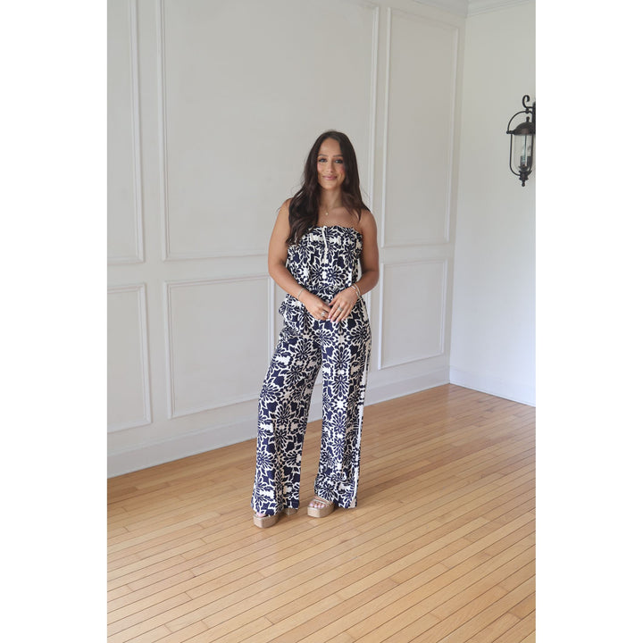 Woman wearing a black and white patterned strapless jumpsuit in a room with wooden flooring and white walls.
