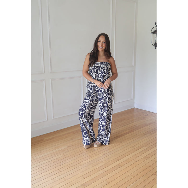 Woman wearing a patterned strapless top and pants in a room with wooden flooring and white walls.