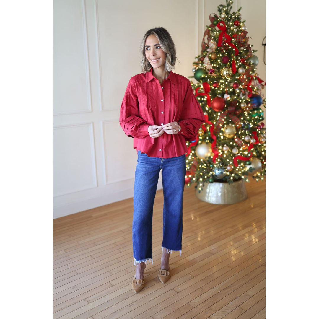 Woman in a red shirt and blue jeans standing in front of a decorated Christmas tree.