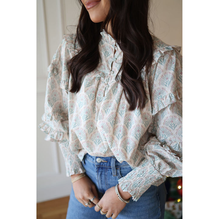 Woman wearing a floral blouse with ruffled sleeves and blue jeans indoors.
