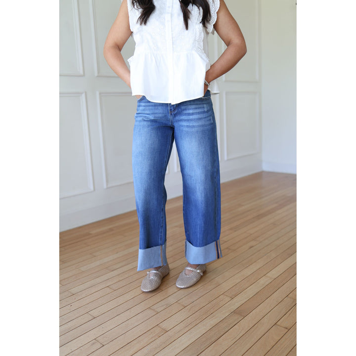 Person wearing blue jeans and a white top on a wooden floor.
