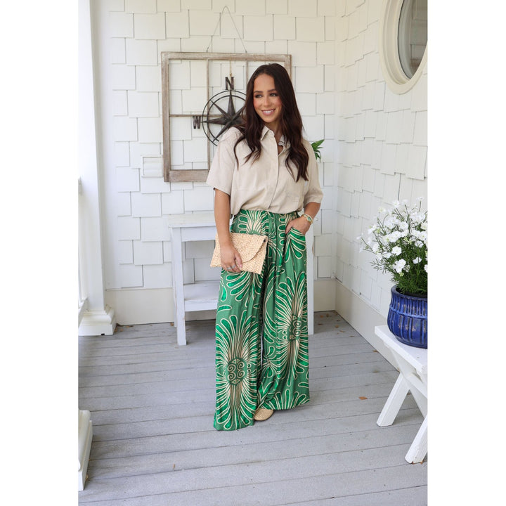 Woman in a beige shirt and green patterned pants standing on a wooden deck.