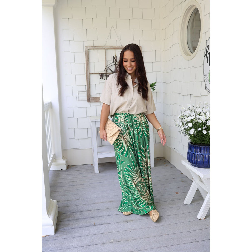 Woman in a beige shirt and green patterned pants standing on a wooden deck.
