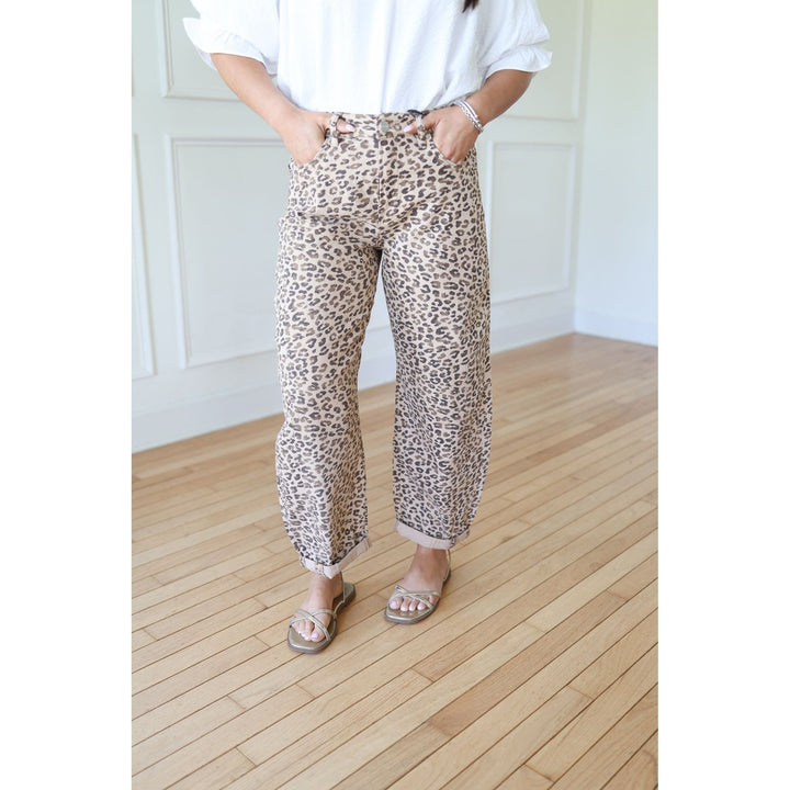 Person wearing leopard print pants and a white top on a wooden floor.