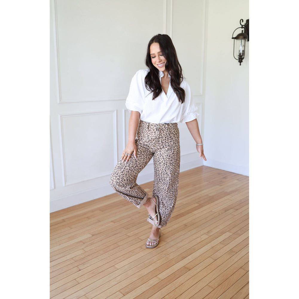 Woman wearing a white blouse and leopard print pants standing on a wooden floor.