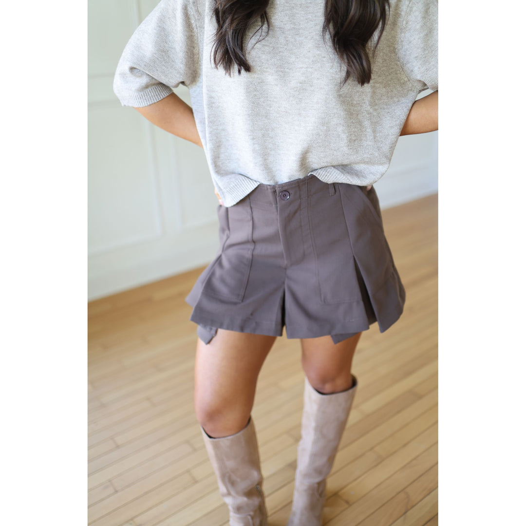 Person wearing a light mocha sweater, brown skirt, and beige knee-high boots 