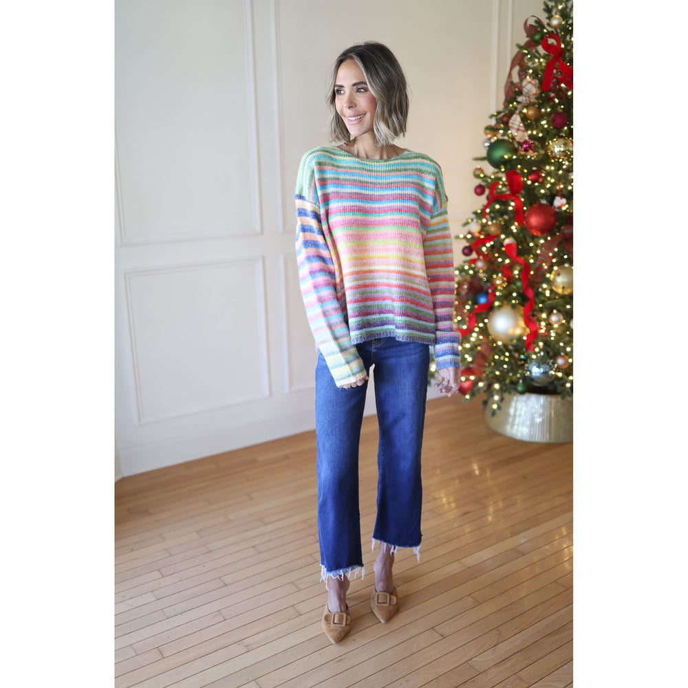 Woman wearing a colorful striped sweater and blue jeans standing in front of a decorated Christmas tree.