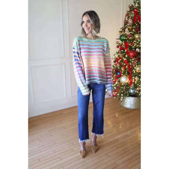 Woman wearing a colorful striped sweater and blue jeans standing in front of a decorated Christmas tree.