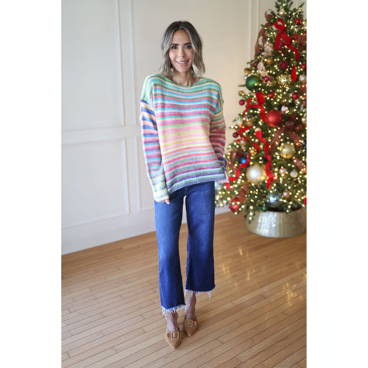 Woman wearing a colorful striped sweater and blue jeans standing in front of a decorated Christmas tree.
