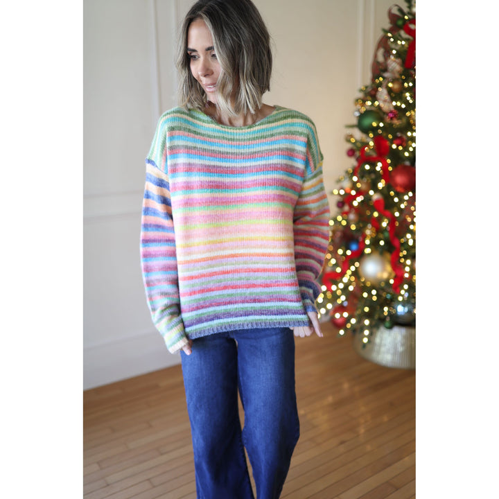 Woman wearing a colorful striped sweater in front of a decorated Christmas tree.