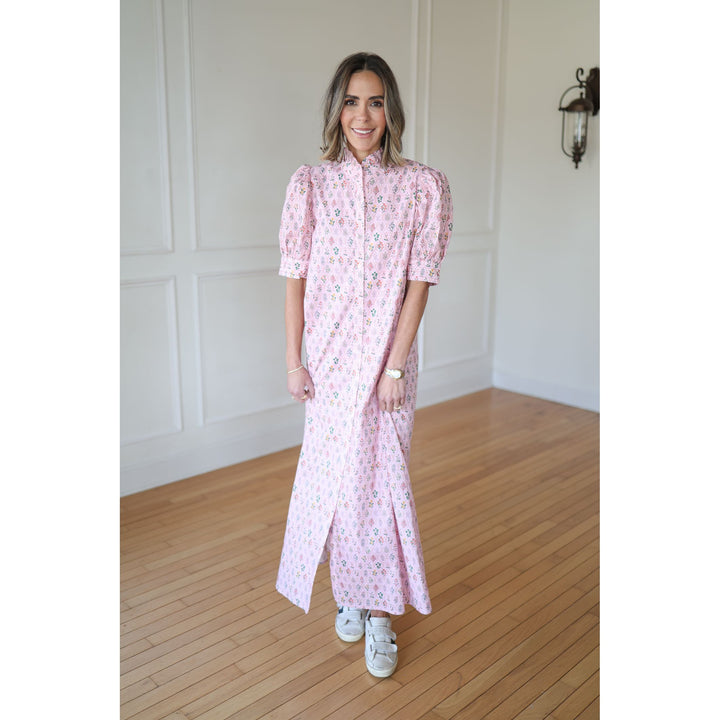 Woman wearing a pink patterned dress standing on a wooden floor with a white wall background