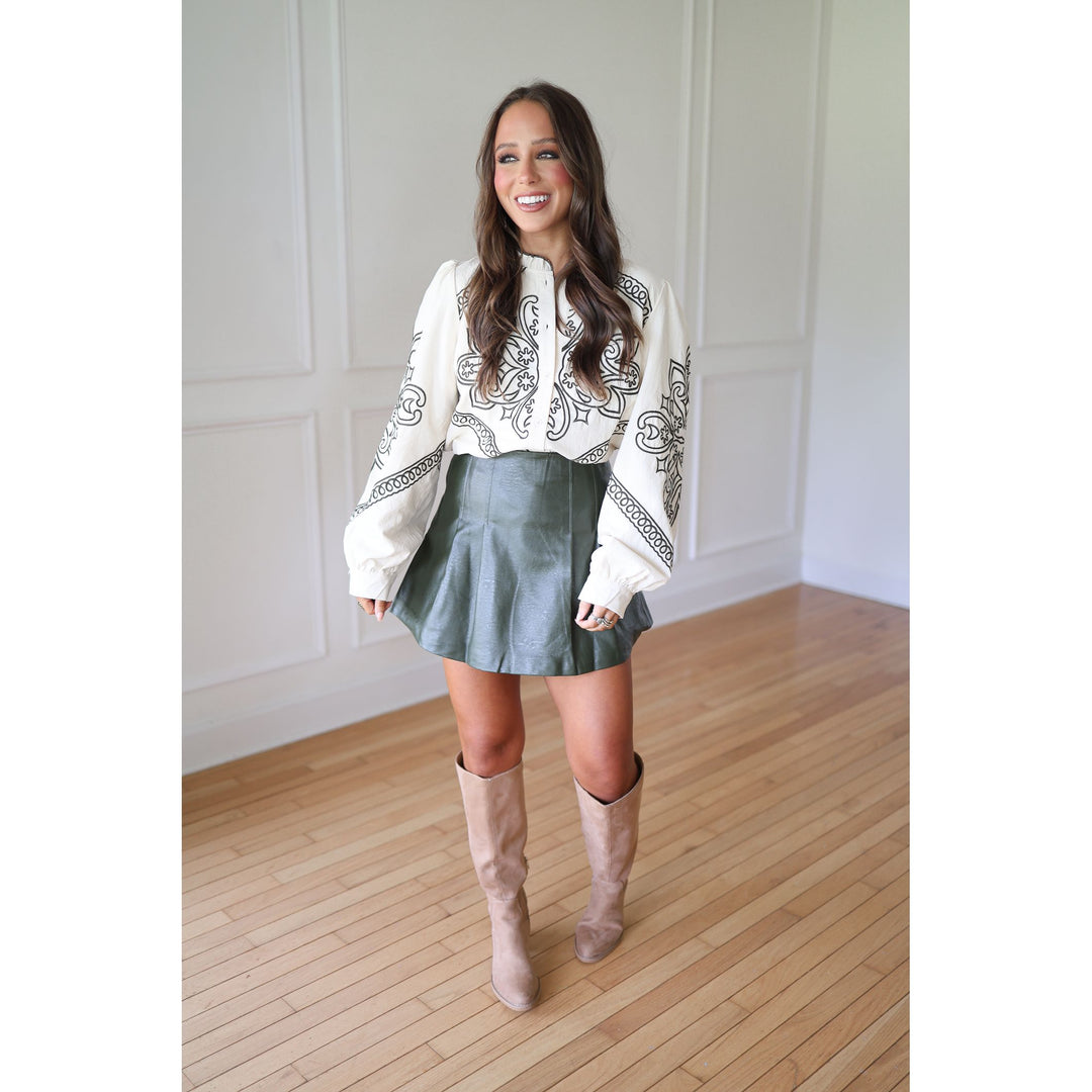 Woman wearing a white blouse with green patterns, green skirt, and beige knee-high boots 