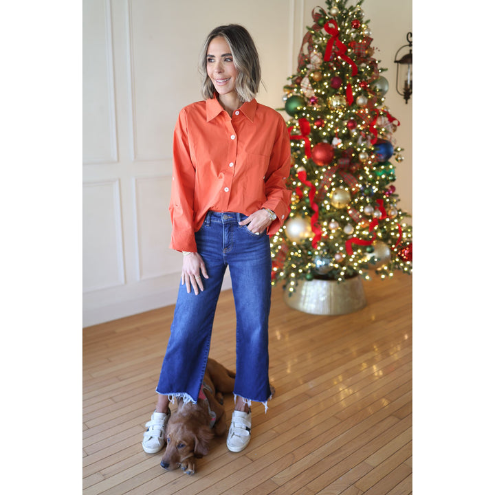 Woman in an orange shirt and blue jeans standing in front of a decorated Christmas tree.