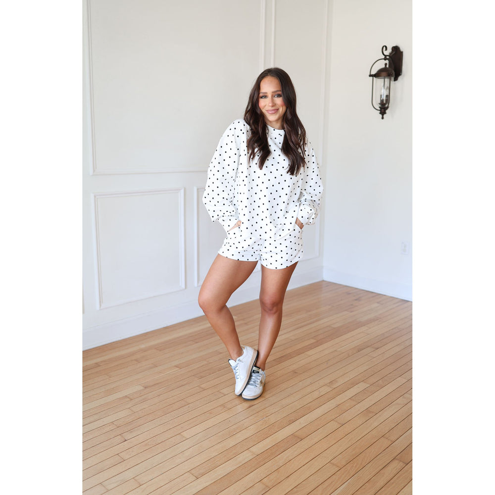 Woman in a polka dot set standing in a room with wooden flooring and white walls.