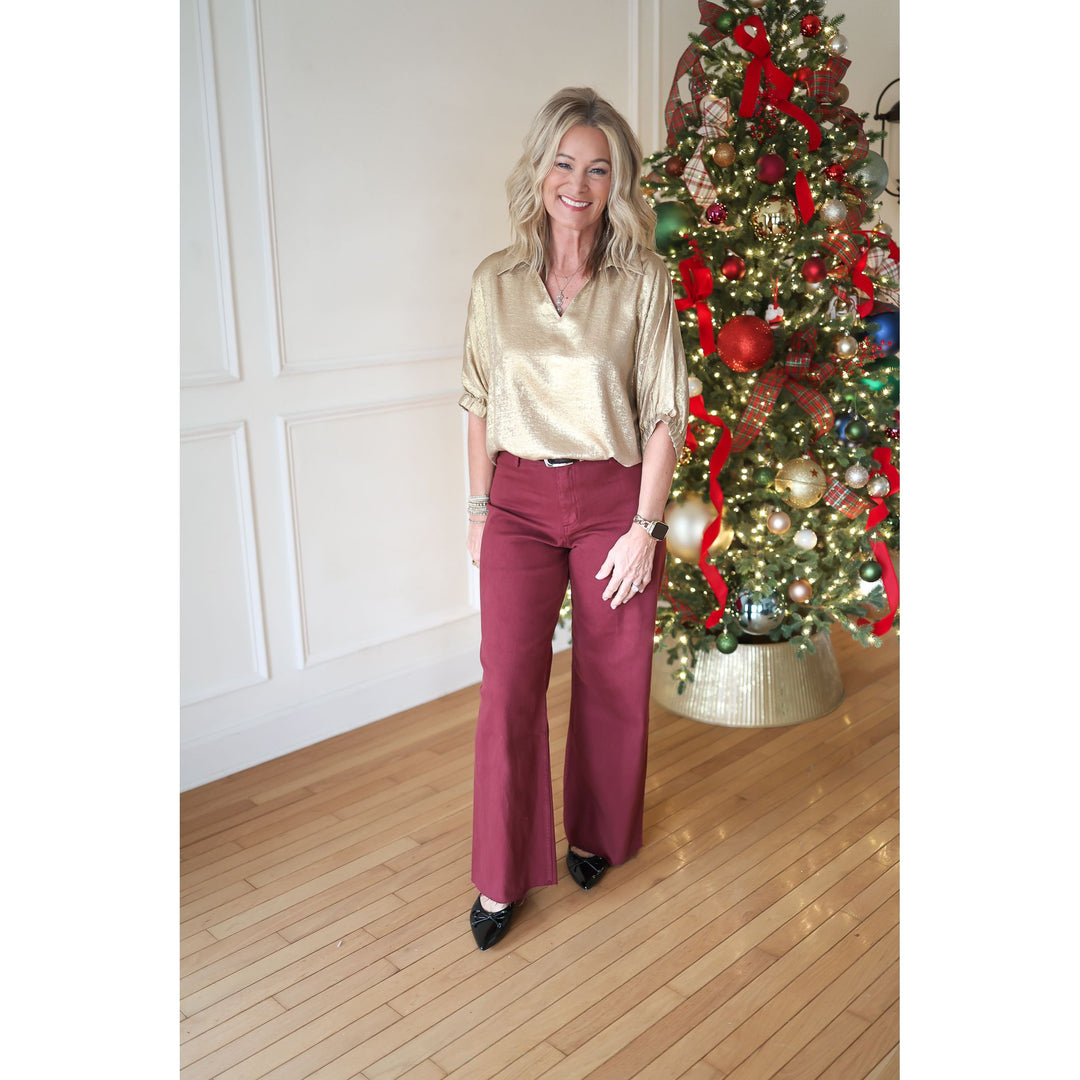 Woman in gold blouse and red pants standing in front of a decorated Christmas tree.