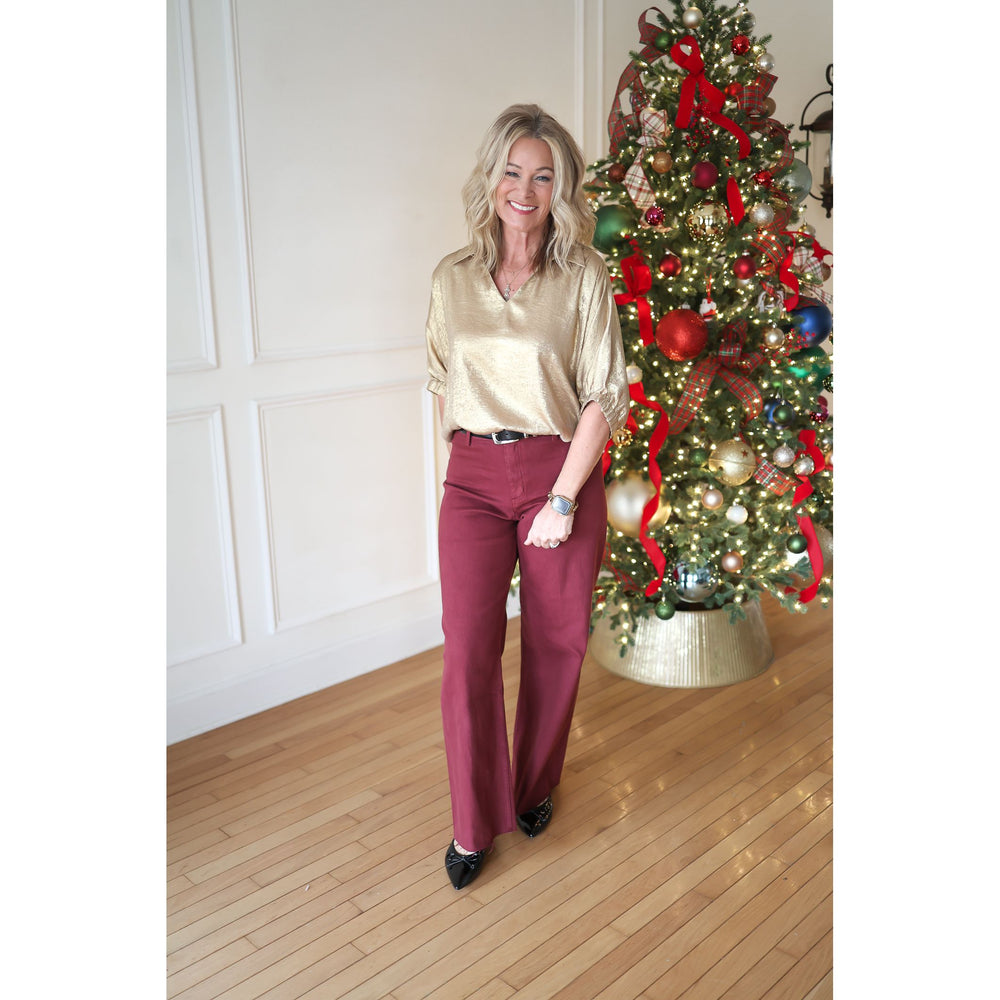 Woman in gold blouse and red pants standing in front of a decorated Christmas tree.