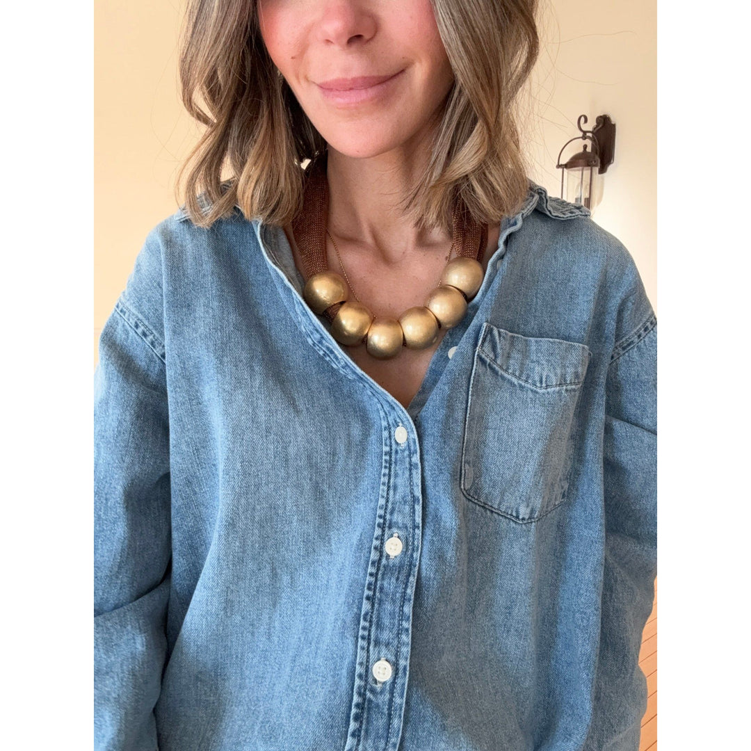 Woman wearing a blue denim shirt and gold necklace against a beige background