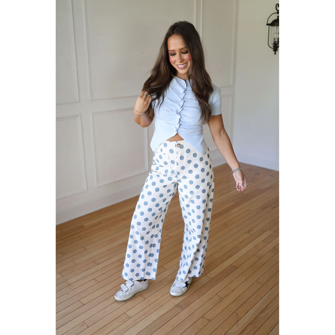 Woman wearing a light blue ruffled top and white pants with blue polka dots 