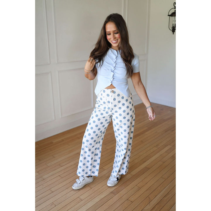 Woman wearing a light blue ruffled top and white pants with blue polka dots 