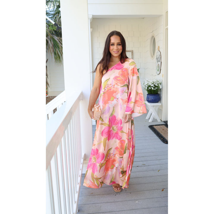 Woman wearing a floral one-shoulder dress on a porch.