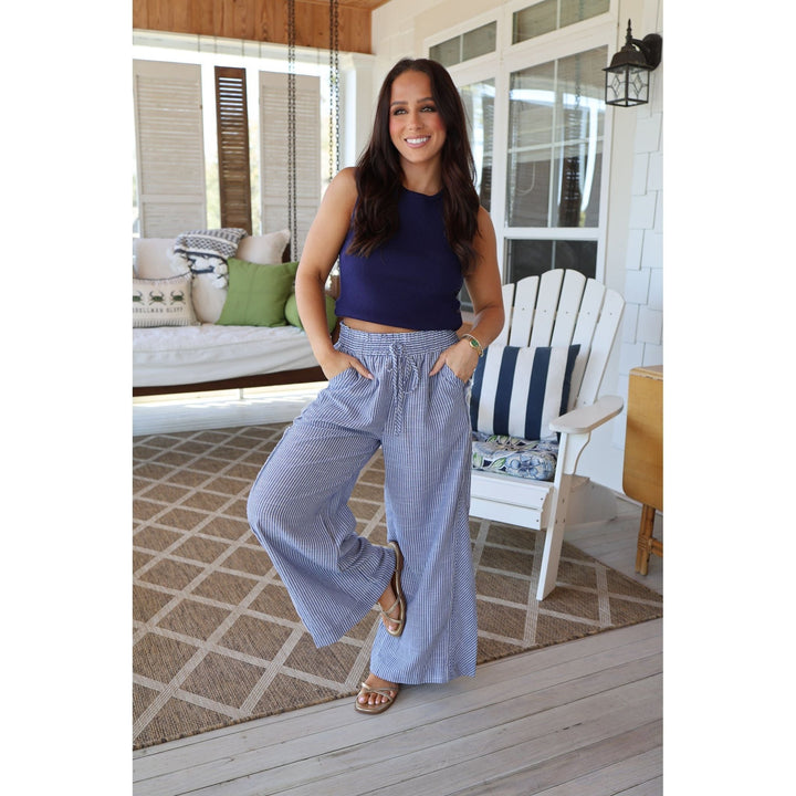 Woman in a blue top and striped pants standing on a porch.
